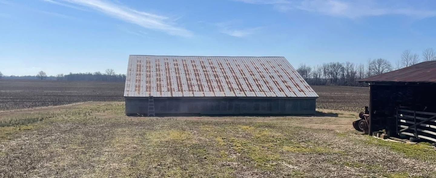 Low-pitch barn in an open field with rust stripes along every panel