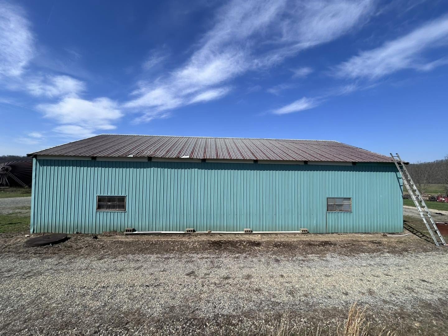 Teal steel building with a faded, rust-brown metal roof before coating
